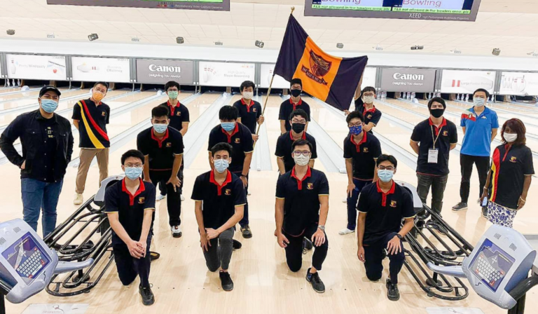 The ACS(I) bowling team poses with a school flag and bowling bags at a bowling alley